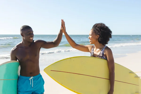 幸せなアフリカ系アメリカ人のカップルは 海で日当たりの良いビーチでサーフボードを高く持っています 健康的なライフスタイル スポーツ サーフィンや休暇 変更なし — ストック写真
