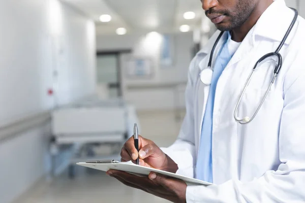 Médico Americano Africano Vestindo Jaleco Estetoscópio Segurando Prancheta Escrevendo Hospital — Fotografia de Stock