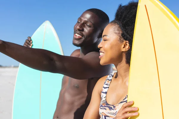 幸せなアフリカ系アメリカ人のカップルは 日当たりの良いビーチで話して立ってサーフボードを保持 健康的なライフスタイル スポーツ サーフィンや休暇 変更なし — ストック写真