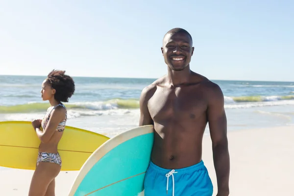 女性サーファーと日当たりの良いビーチに立ってサーフボードを保持幸せなアフリカ系アメリカ人男性の肖像画 健康的なライフスタイル スポーツ サーフィンや休暇 変更なし — ストック写真
