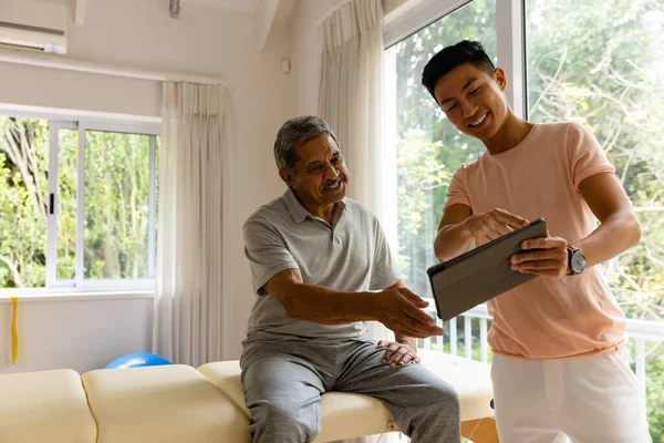 Happy Diverse Male Physiotherapist Examining Senior Male Patient Using Tablet — Stock Photo, Image
