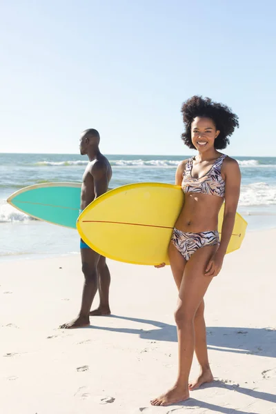 男性サーファーと日当たりの良いビーチに立ってサーフボードを保持幸せなアフリカ系アメリカ人女性の肖像画 健康的なライフスタイル スポーツ サーフィンや休暇 変更なし — ストック写真