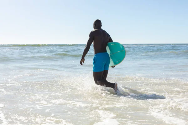 日当たりの良いビーチを歩いて海にサーフボードを運ぶアフリカ系アメリカ人の男に合う 健康的なライフスタイル スポーツ サーフィンや休暇 変更なし — ストック写真