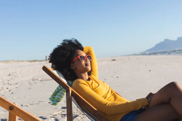 戴着太阳镜的快乐的非洲裔美国女人躺在阳光充足的海滩上的躺椅上放松 闲暇时间和假期 — 图库照片