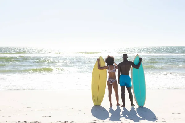 海に面した日当たりの良いビーチに立ってサーフボードとアフリカ系アメリカ人のカップルの背面ビュー コピースペース 健康的なライフスタイル スポーツ サーフィンや休暇 変更なし — ストック写真