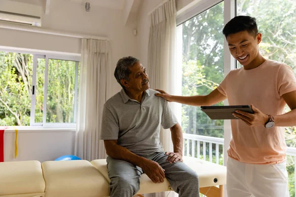 Feliz Fisioterapeuta Masculino Diverso Examinando Paciente Masculino Mayor Usando Tableta —  Fotos de Stock