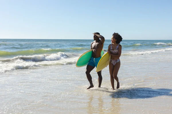 Szczęśliwa Wysportowana Afrykańska Para Niosąca Deski Surfingowe Spacerujące Słonecznej Plaży — Zdjęcie stockowe