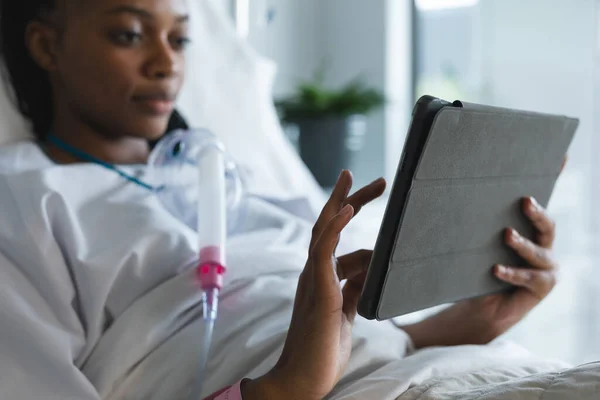 アフリカ系アメリカ人女性の患者がベッドに横になり 病院の部屋でタブレットを使用している コミュニケーション 医療と仕事 変更なし — ストック写真