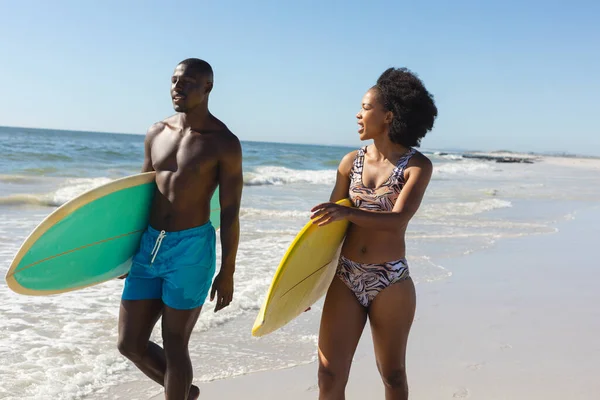 健康的非洲裔美国夫妇背着冲浪板聊天 走在海边阳光明媚的海滩上 健康的生活方式 业余爱好 冲浪和度假 — 图库照片