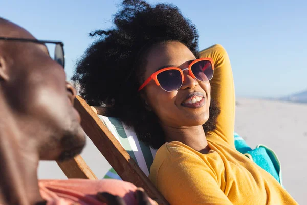 快乐的非洲裔美国夫妇 戴着太阳镜 坐在躺椅上 在阳光灿烂的海滩上微笑 聚会和度假 — 图库照片