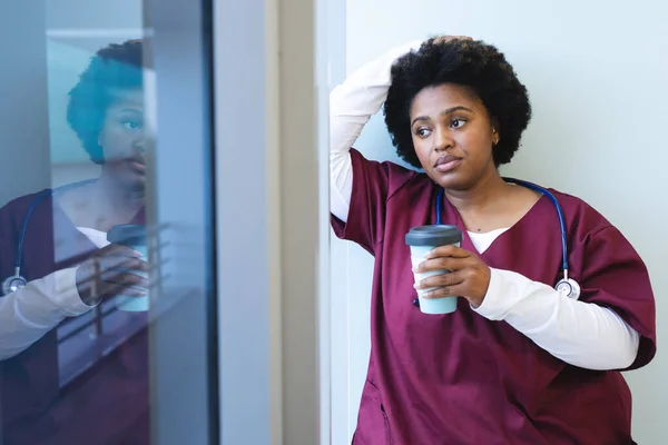 頭の良いアフリカ系アメリカ人の女性医師は スクラブを着用し コーヒーを持ち 窓から見ています 医療と仕事 変更なし — ストック写真