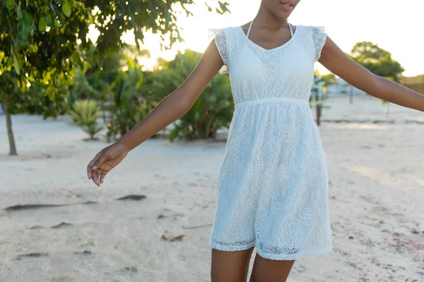 白いビーチのドレスでアフリカ系アメリカ人の女性の中央部は日当たりの良いビーチで踊る リラクゼーションと休暇 変わらない — ストック写真