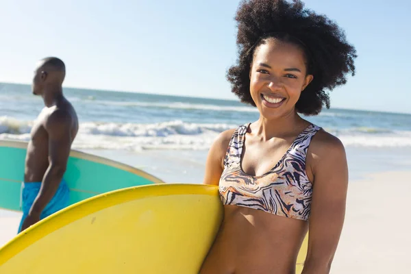 与男性冲浪运动员一起站在阳光灿烂的海滩上的快乐的非洲裔美国女人的画像 健康的生活方式 业余爱好 冲浪和度假 — 图库照片