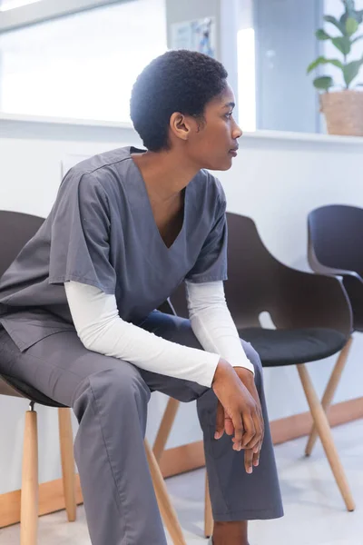 Trött Afrikansk Amerikansk Kvinnlig Läkare Klädd Skrubb Sittande Stol Korridoren — Stockfoto