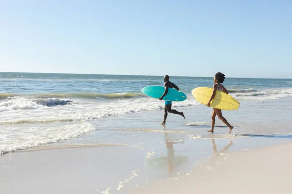 非洲裔美国人夫妇背着冲浪板在阳光灿烂的海滩上奔向大海 复制空间 健康的生活方式 业余爱好 冲浪和度假 — 图库照片