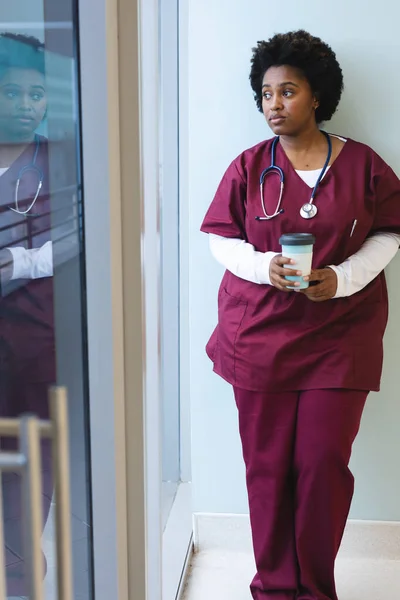 富有洞察力的非洲裔美国女医生 戴着刷子 拿着咖啡 从窗户往外看 保健和工作 — 图库照片