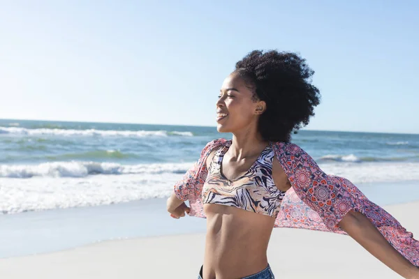 幸せなアフリカ系アメリカ人女性が笑顔で海沿いの日当たりの良いビーチを歩いています リラックスと休暇 変更なし — ストック写真