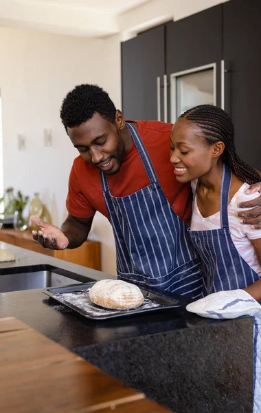 台所で焼きパンを抱きかかえ 楽しむエプロンの幸せなアフリカ系アメリカ人のカップル ライフスタイル 団結と国内生活 変更されない — ストック写真