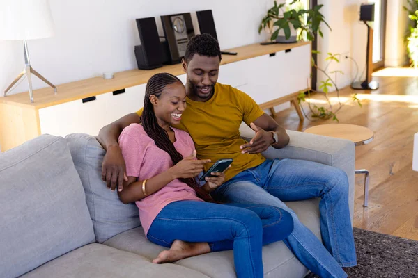 Glad Afrikansk Amerikansk Par Leende Omfamna Och Använda Smartphone Soffan — Stockfoto