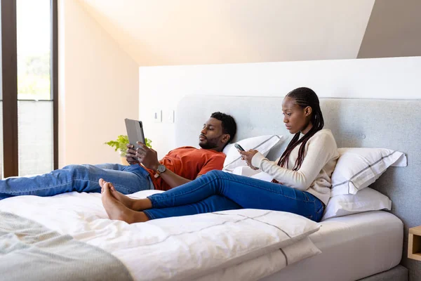 使用平板电脑和智能手机的非洲裔美国人夫妇躺在卧室的床上 生活方式 沟通和家庭生活 — 图库照片
