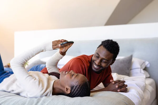 寝室に寝そべっているスマートフォンを使ってアフリカ系アメリカ人の幸せなカップル リラクゼーション ライフスタイル 一緒に コミュニケーションと国内生活 変更なし — ストック写真