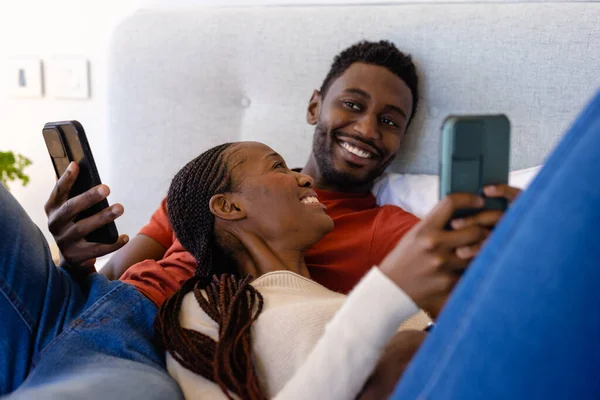Ευτυχισμένο Ζευγάρι Αφροαμερικανών Που Χρησιμοποιούν Smartphones Ξαπλωμένοι Στο Κρεβάτι Στην — Φωτογραφία Αρχείου