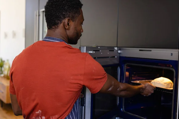 アフリカ系アメリカ人の男がパン生地をキッチンのオーブンに入れている ライフスタイル 家庭生活 変わらない — ストック写真