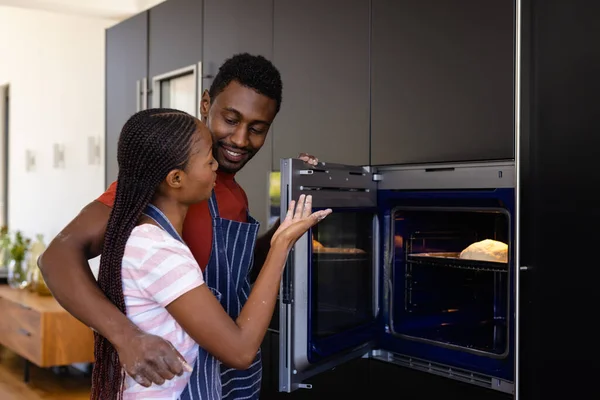 台所でオーブンを使用してパンを焼くエプロンの幸せなアフリカ系アメリカ人のカップル ライフスタイル 団結と国内生活 変更されない — ストック写真
