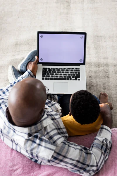 stock image African american grandfather and grandson sitting on sofa, using laptop with copy space on screen. Family, lifestyle, childhood, togetherness, communication, free time and domestic life, unaltered.