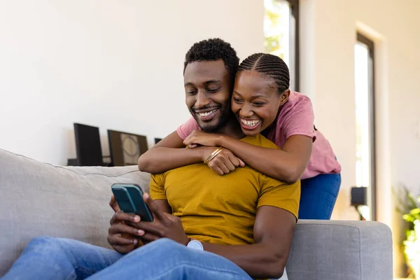 幸せなアフリカ系アメリカ人のカップルは 自宅でソファの上でスマートフォンを受け入れ 使用して笑顔 ライフスタイル コミュニケーション 愛と国内生活 変わらない — ストック写真