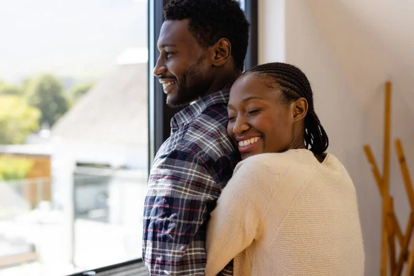 幸せなアフリカ系アメリカ人の夫婦が家で窓から抱きついている ライフスタイル 団結と国内生活 変わらない — ストック写真