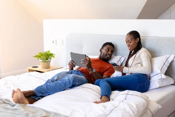 快乐的非洲裔美国夫妇使用平板电脑和智能手机躺在床上卧室里 生活方式 沟通和家庭生活 — 图库照片