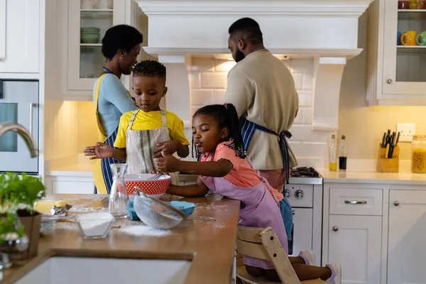 非洲裔美国兄弟姐妹在厨房岛上的碗中搅拌面糊 父母在背景中做饭 不变的 — 图库照片