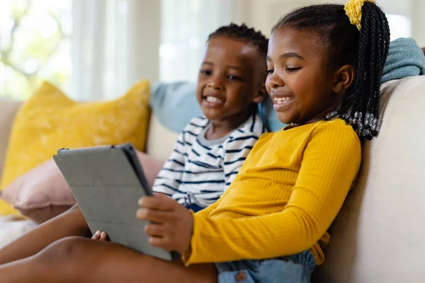 快乐的非洲裔美国姐姐和兄弟坐在客厅的沙发上 用数字平板电脑 无线技术和家庭观念 — 图库照片