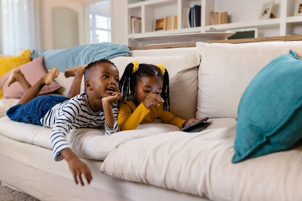 非裔美国人兄弟姐妹躺在沙发上 在客厅里用数字平板电脑 无线技术和家庭观念 — 图库照片