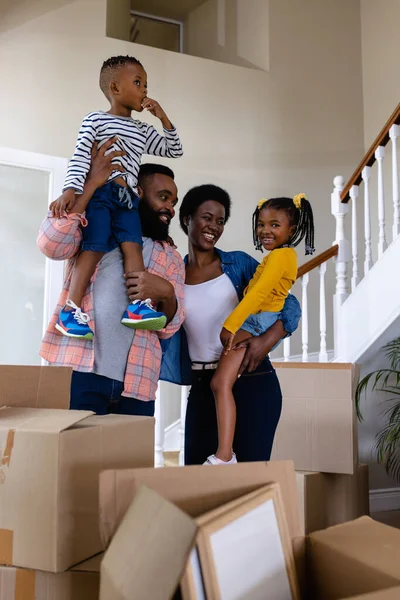 新しい家の箱のそばに立っている間に子供を運んでいるアフリカ系アメリカ人の両親 変更されていない 子供時代 引っ越しの家と移転の概念 — ストック写真