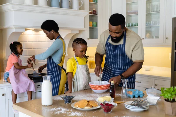 非裔美国人的父亲和儿子在碗里搅拌面糊 而母亲和女儿则在煮煎饼 不变的生活方式 烹调和厨房 — 图库照片