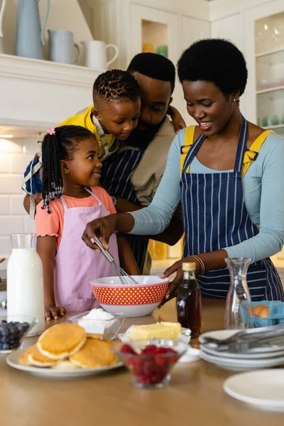 儿子和女儿的非裔美国父亲看着母亲在厨房的碗里搅拌面糊 不变的生活方式 准备和学习概念 — 图库照片