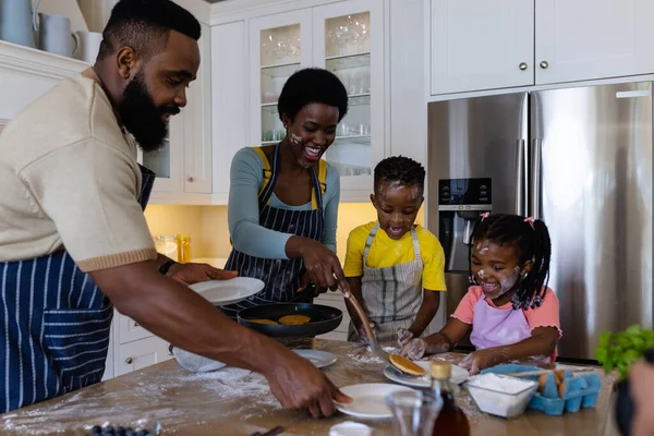乱雑なキッチン島で遊び心のある子供たちにパンケーキを提供する陽気なアフリカ系アメリカ人の両親 変更されていない ライフスタイル 一緒に 子供時代 食べ物 幸せと家庭の概念 — ストック写真