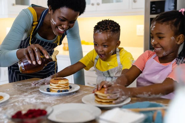 Счастливая Африканская Американская Мать Наливает Мёд Блинчики Которые Подают Детям — стоковое фото