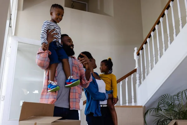 新しい家の箱のそばに立っている間に子供を運んでいるアフリカ系アメリカ人の両親の低い角度の眺め 変更されていない 子供時代 引っ越しの家と移転の概念 — ストック写真
