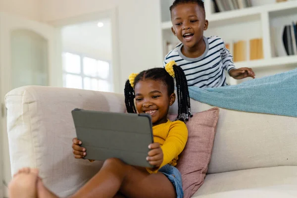 Menino Afro Americano Espreitando Irmã Feliz Usando Tablet Digital Sofá — Fotografia de Stock