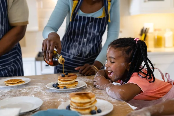 一个好奇的非裔美国女孩张大嘴看着妈妈把蜂蜜倒在盘子里的煎饼上 不变的生活方式 诱惑和厨房 — 图库照片