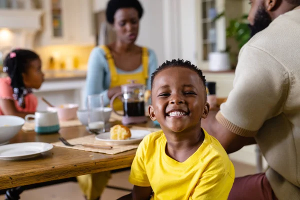 非裔美国男孩一边和家人一起在餐桌边吃早餐 一边微笑着看着相机 不变的生活方式 早晨和家庭观念 — 图库照片