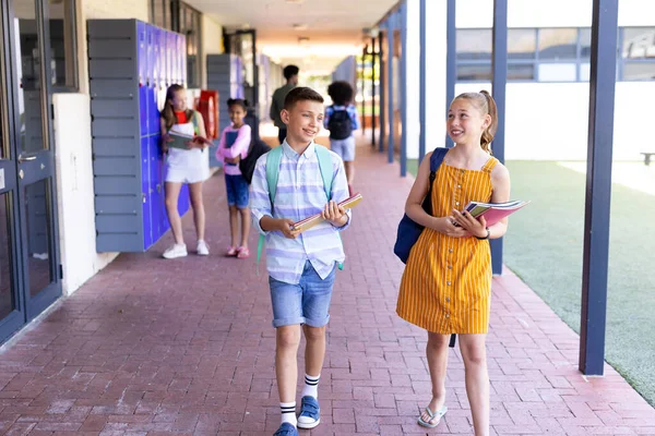 笑容满面的男孩和女孩拿着书本 走在学校走廊里交谈着抄袭空间 小学和学习概念 — 图库照片