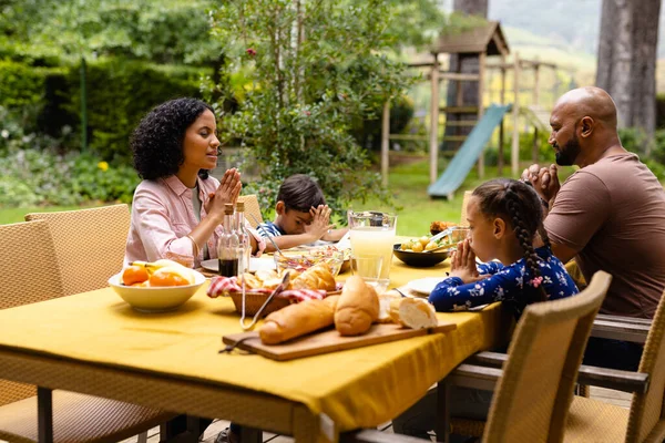 快乐的父母 儿子和女儿在饭前祈祷 坐在阳光灿烂的花园的桌旁 食物和生活方式 — 图库照片