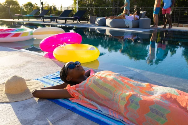 快乐的非洲裔美国女人躺在花园游泳池旁边的毛巾和日光浴中 生活方式 业余时间和假期 — 图库照片