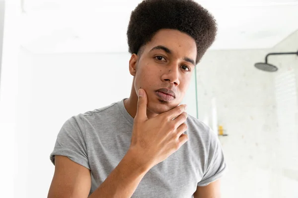 Homem Biracial Olhando Espelho Inspecionando Rosto Pele Banheiro Ensolarado Autocuidado — Fotografia de Stock
