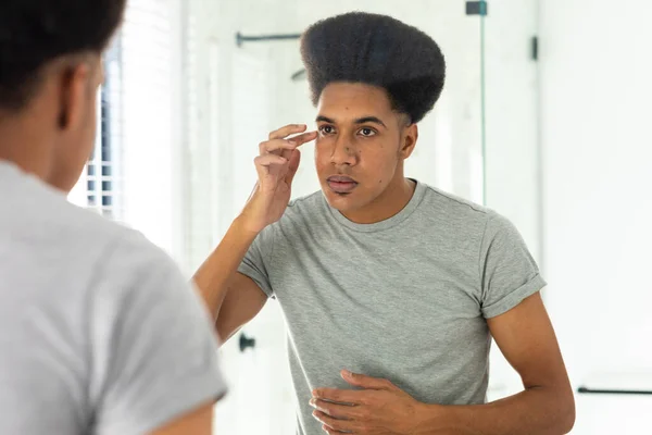 Hombre Biracial Mirando Espejo Inspeccionando Cara Los Ojos Baño Soleado — Foto de Stock