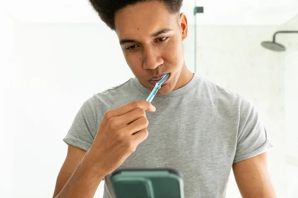 Biracial Pria Menggosok Gigi Dan Menggunakan Smartphone Kamar Mandi Cerah — Stok Foto